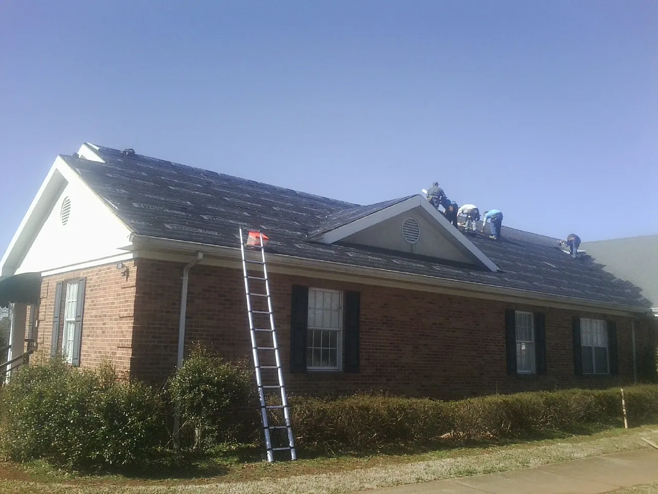 Crew tearing shingles off a brick ranch roof with a ladder set — Emergency Roof Repair work by our crew in Jefferson