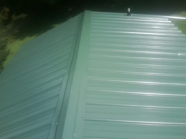New green metal panels meeting at the ridge of a roof — Flat Roof Repair work by our crew in Jefferson