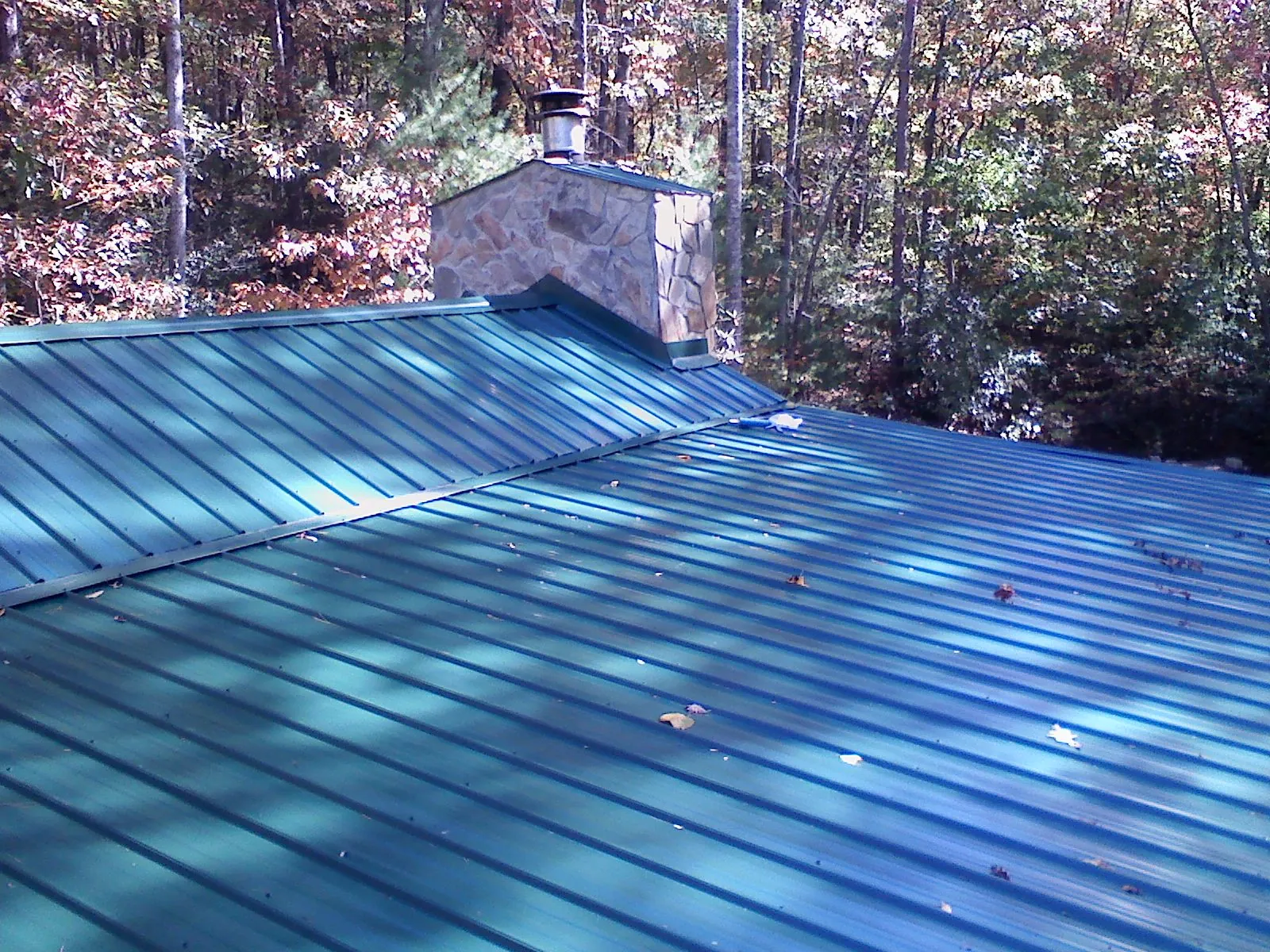 New green metal roof and stone chimney surrounded by autumn woods in Jefferson